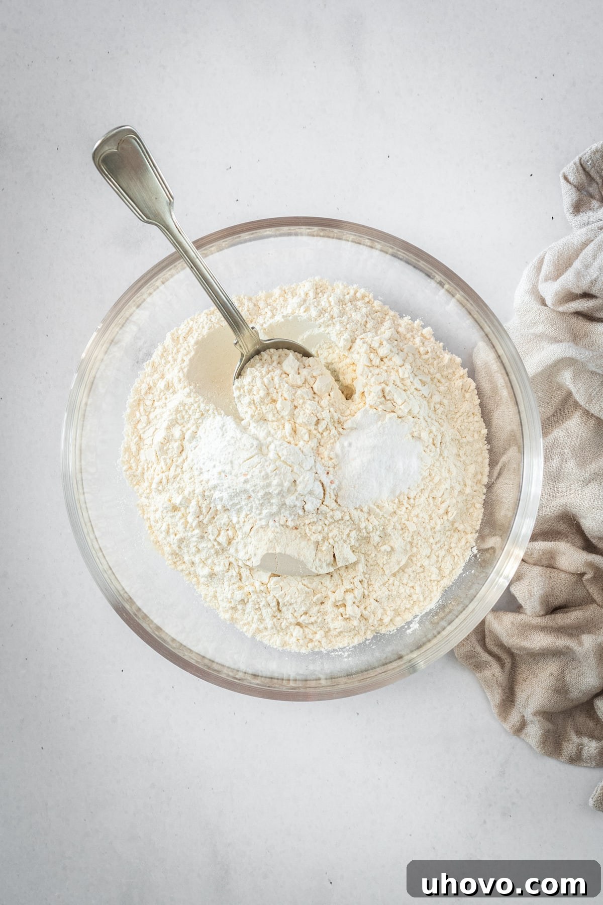 An overhead shot of dry cake ingredients (flour, baking powder, baking soda, salt) perfectly whisked together in a clear glass bowl.