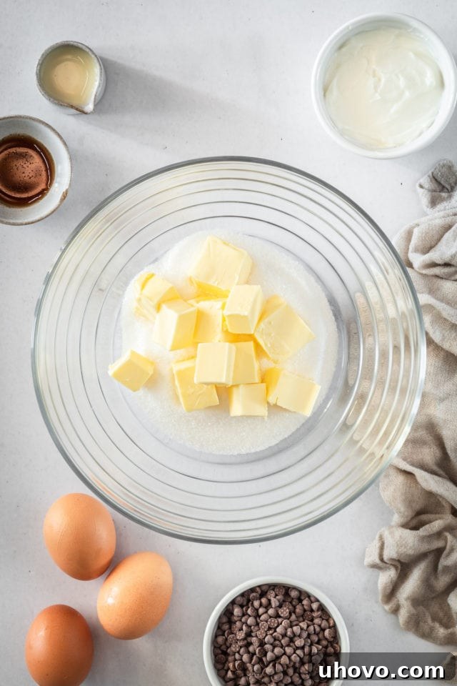 Overhead shot of softened butter and granulated sugar ready to be creamed in a glass bowl.