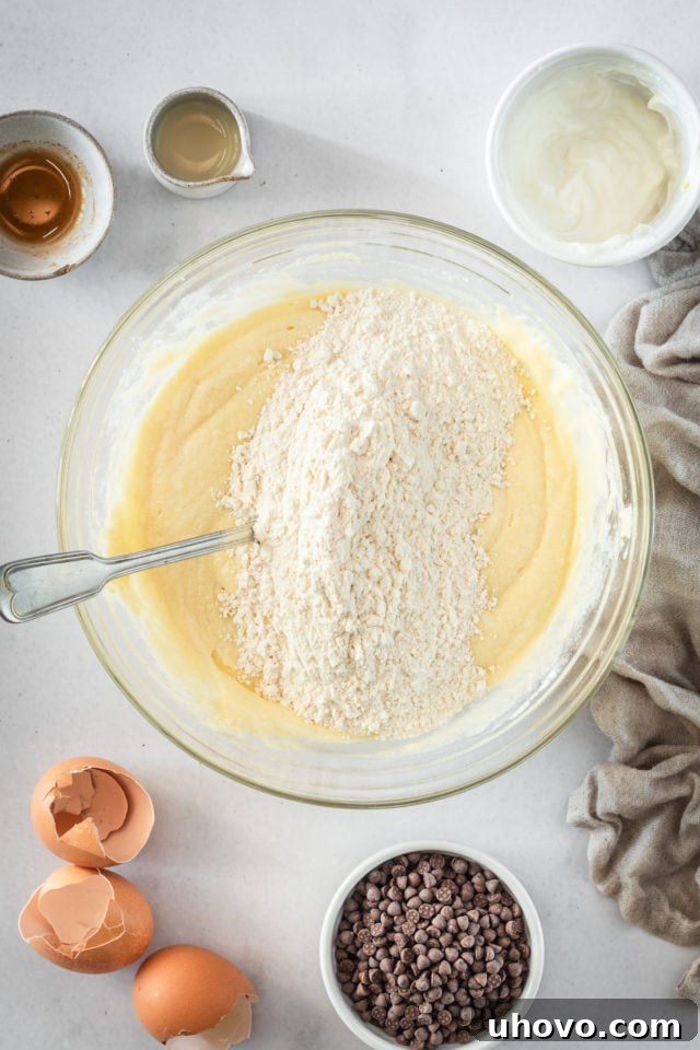 An overhead shot illustrating the gradual incorporation of flour into the Chocolate Chip Cake batter in a glass bowl.