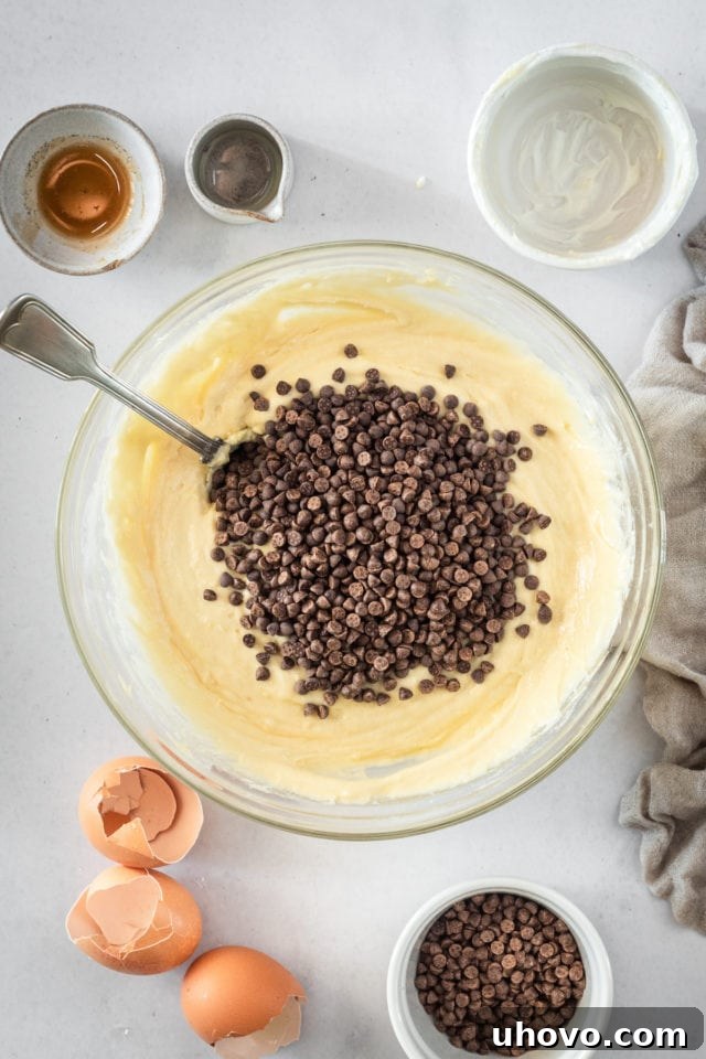 An overhead shot showing chocolate chips being gently folded into the cake batter using a spatula, ensuring even distribution.