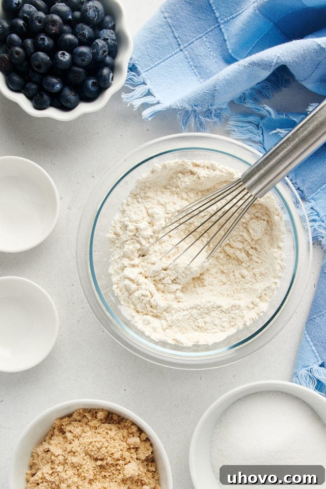 Overhead view of dry ingredients (flour, baking powder, salt) in a mixing bowl, being whisked together with a metal whisk.