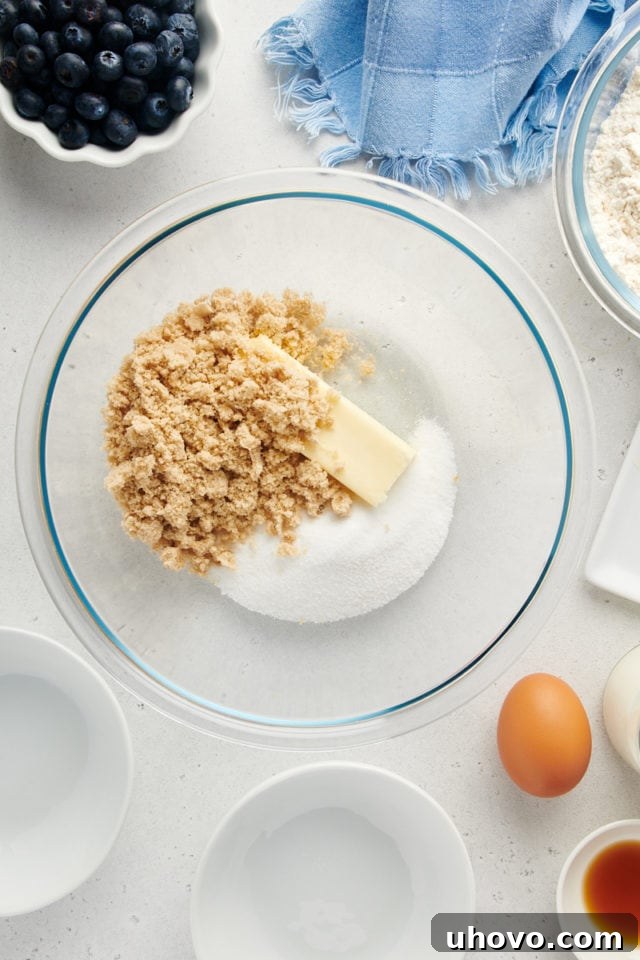 Overhead shot of softened butter, granulated sugar, and light brown sugar being creamed together in a mixing bowl using an electric mixer.