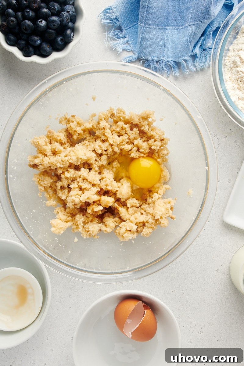 Overhead view of a single egg cracked into a bowl of creamed butter and sugar, ready to be mixed.