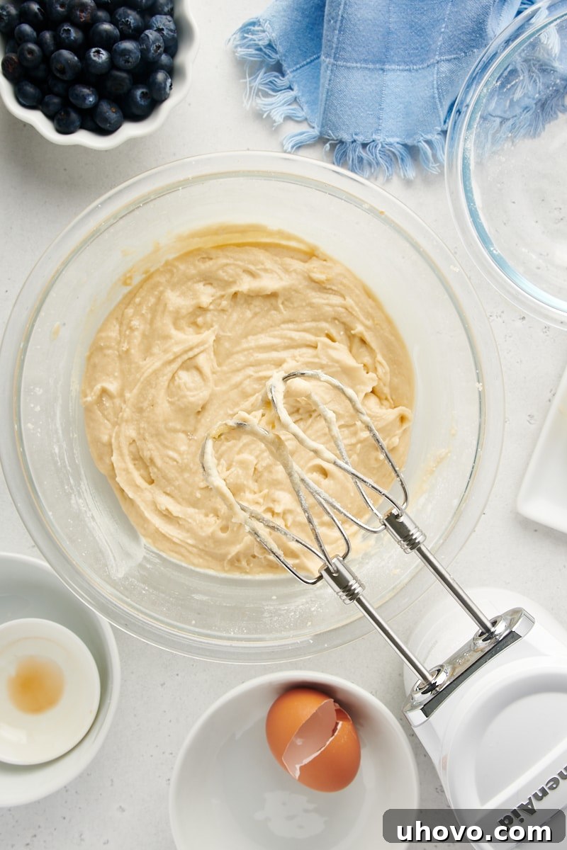 Overhead view of cake batter in a mixing bowl with a hand mixer, showing the gradual incorporation of flour and milk.