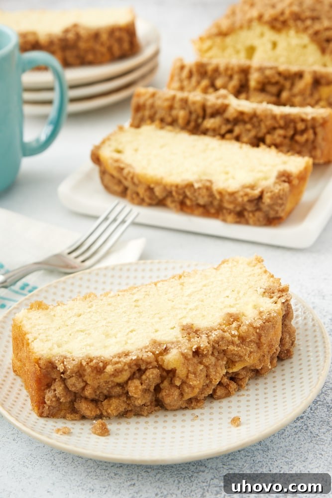 A perfectly portioned slice of Sour Cream Coffee Cake, revealing its moist interior and generous crumb topping, presented on an elegant white and beige plate.