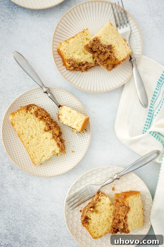 An artistic overhead arrangement of multiple slices of Sour Cream Coffee Cake, each perfectly cut and displayed on an assortment of white and beige plates.