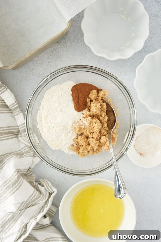 An overhead shot showing the dry ingredients for the crumb topping – brown sugar, flour, and cinnamon – neatly arranged in a glass bowl, awaiting mixing.