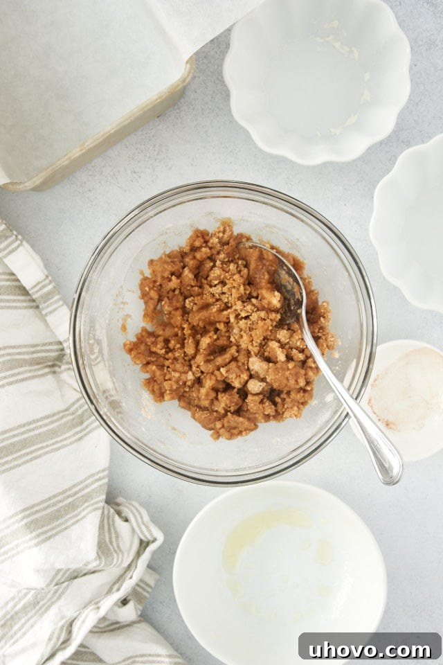 A close-up view of the perfectly formed, moist crumb topping resting in a clear glass mixing bowl, ready to be sprinkled over the coffee cake batter.