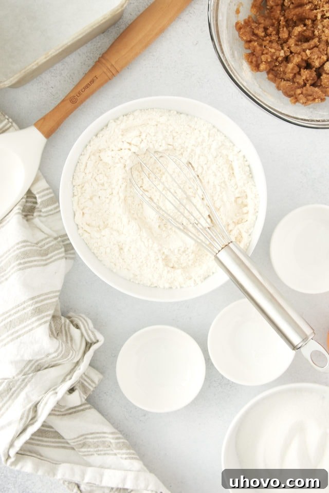 A glass mixing bowl filled with the precisely measured dry ingredients for the coffee cake – flour, baking powder, baking soda, and salt – whisked together.