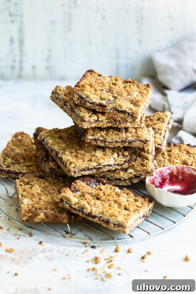 Raspberry bars stacked on wire rack with small bowl of jam