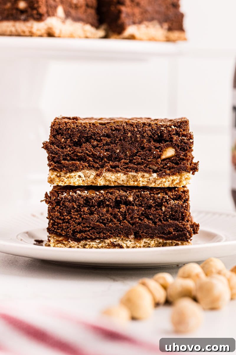Two rich Nutella brownies, stacked on a white plate, showcasing the distinct shortbread crust layer.