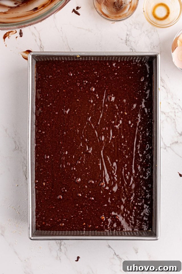 Overhead view of the rich brownie batter being spread evenly over the pre-baked shortbread crust in the pan.