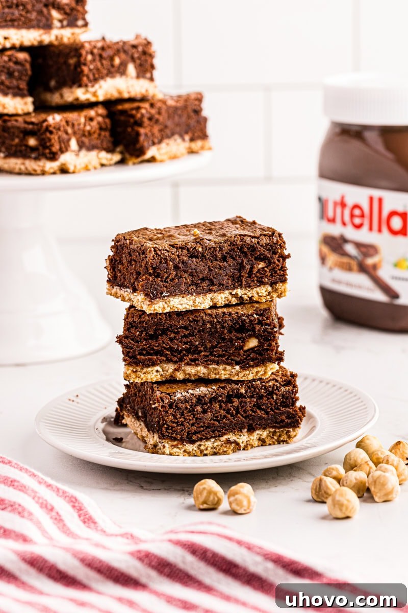 Three perfectly cut Nutella brownies with shortbread crust, stacked neatly on a pristine white plate.