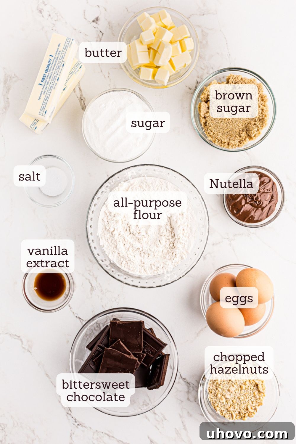 Overhead shot of essential baking ingredients for Nutella shortbread brownies, clearly labeled on a rustic wooden surface.