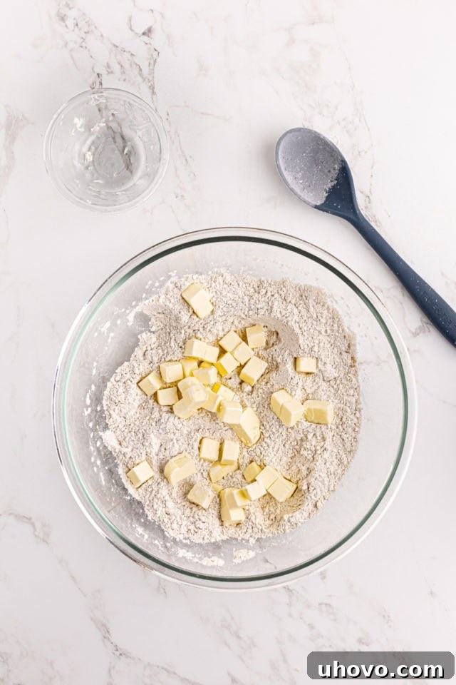 Overhead view of cold butter cubes being incorporated into dry shortbread ingredients.