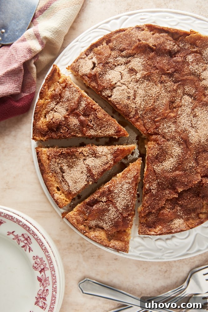 An overhead view of a whole Cinnamon Pear Cake, with a few slices already cut, revealing the moist interior and pear pieces, elegantly presented on a white cake stand.