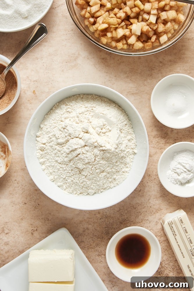 A collection of fresh ingredients neatly arranged on a kitchen counter, ready for baking the Cinnamon Pear Cake. This includes flour, sugar, butter, cream cheese, vanilla extract, eggs, fresh pears, and a small bowl of cinnamon.
