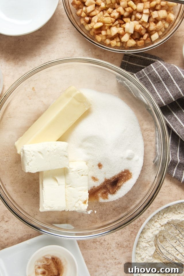 Creaming ingredients for the cake, showing softened butter, granulated sugar, cream cheese, and vanilla extract combined in a clear glass mixing bowl, creating a smooth, light mixture.