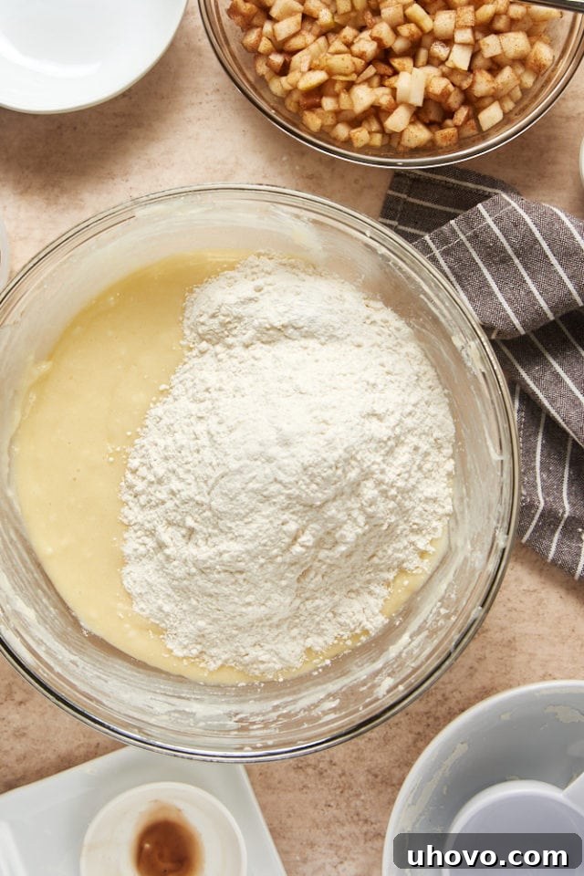 Flour mixture being gradually added to the wet ingredients in a glass mixing bowl, showing the initial stages of combining cake batter.