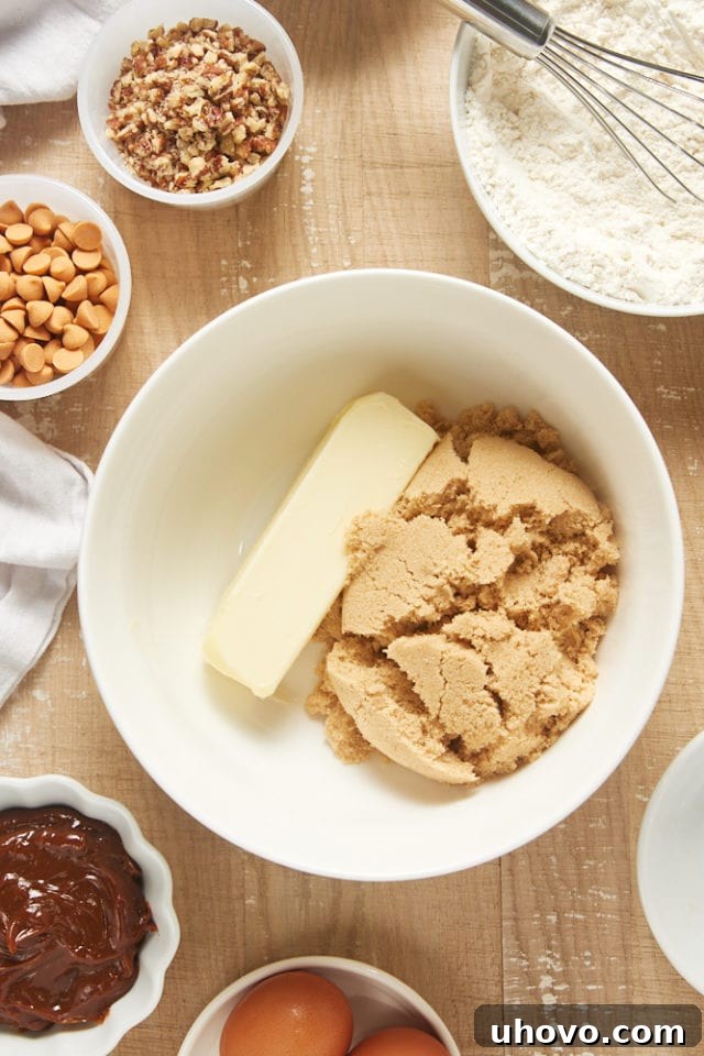Overhead view of butter and brown sugar creaming together in a white mixing bowl, forming a light and fluffy mixture.