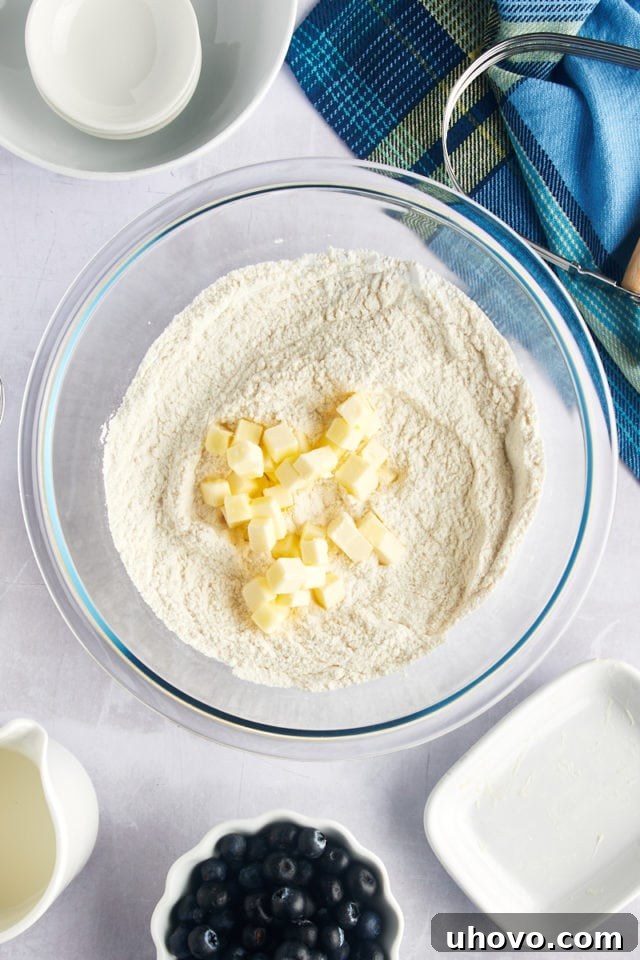 Overhead view of small cubes of softened butter being added to the bowl of whisked dry ingredients for biscuits.