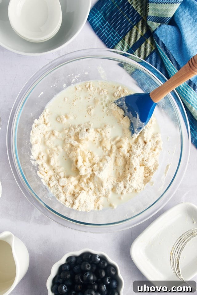 Overhead view of milk being poured into a mixing bowl containing biscuit dough, after sour cream has been added.