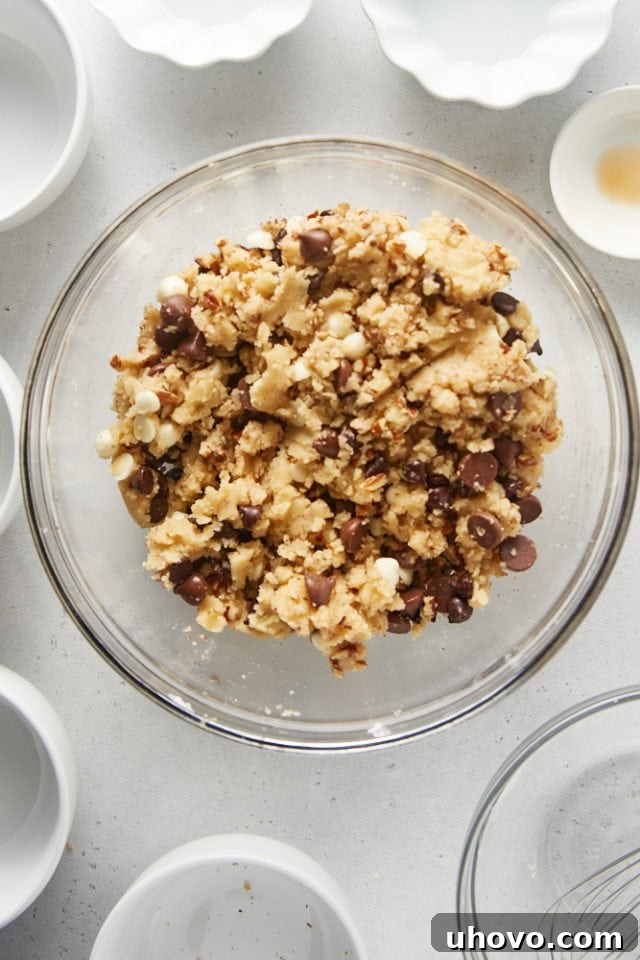 Overhead view of the fully mixed Triple Chocolate Chip Cookie Brittle dough in a glass mixing bowl, with chocolate chips and nuts evenly distributed.