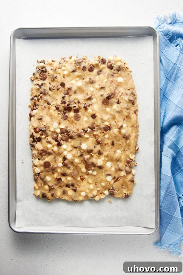 Overhead view of the Triple Chocolate Chip Cookie Brittle dough perfectly shaped into a uniform rectangle on a parchment-lined baking sheet, leaving a slight border.