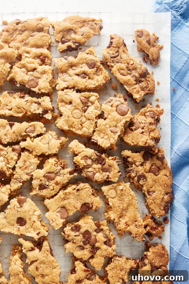 Overhead view of a large piece of Triple Chocolate Chip Cookie Brittle broken into smaller, irregular pieces on a white surface, ready for serving.