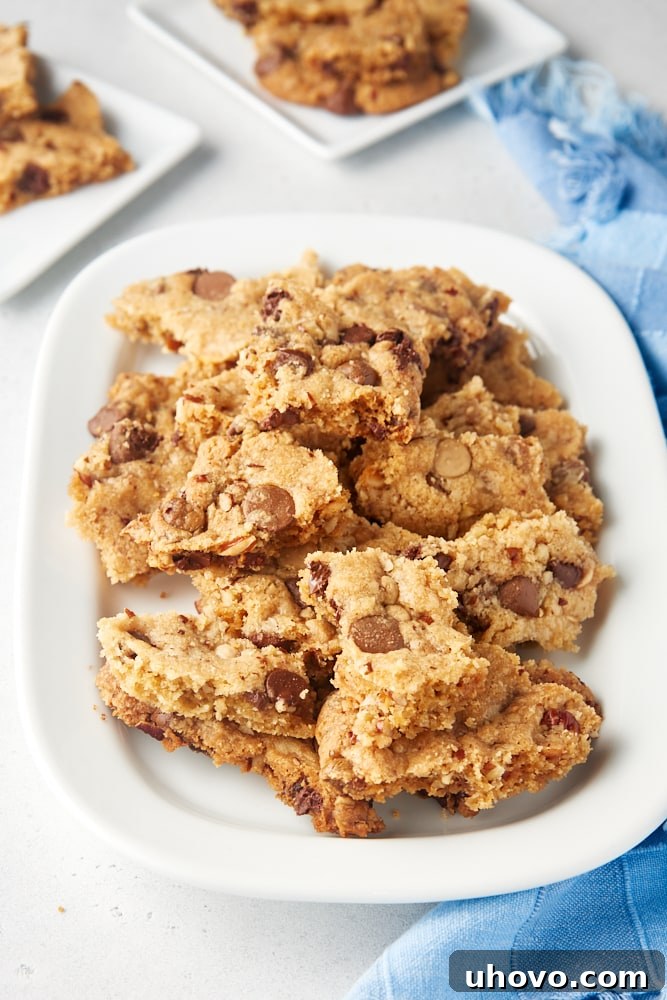 Pile of irregularly shaped Triple Chocolate Chip Cookie Brittle pieces stacked on a pristine white tray, emphasizing their varied textures and chocolate chunks.