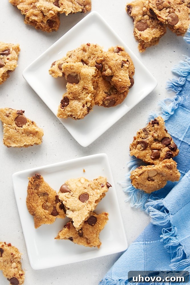 A stack of golden brown Triple Chocolate Chip Cookie Brittle pieces on small white square plates, highlighting their rich color and irregular edges.