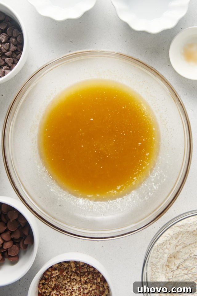 Overhead view of melted butter, granulated sugar, brown sugar, and vanilla extract combined in a glass mixing bowl, creating a smooth, golden mixture.