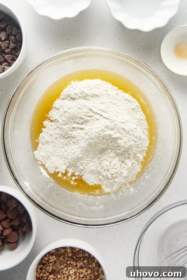 Overhead view of the dry flour mixture being added to the wet butter and sugar mixture in a glass bowl.