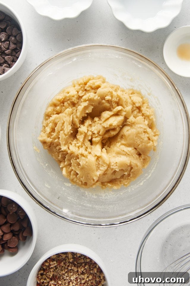 Overhead view of Triple Chocolate Chip Cookie Brittle dough in a glass mixing bowl, showing the flour mostly incorporated with a few streaks remaining.