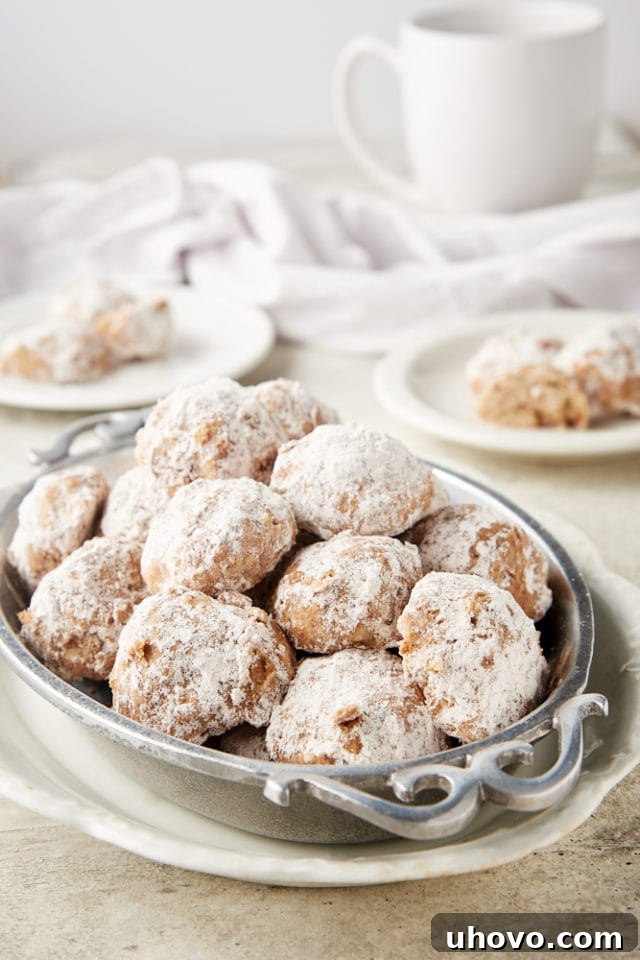 A festive display of Nutty Spiced Snowdrop Cookies nestled in a pewter tray, with additional cookies artfully arranged on white plates in the background, creating a warm, inviting scene.
