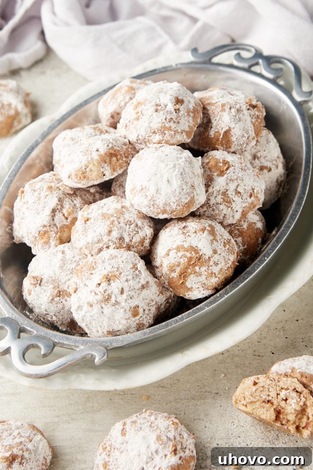 A collection of Nutty Spiced Snowball Cookies elegantly presented in an oval pewter tray, with additional cookies scattered around on a surface, inviting a taste.