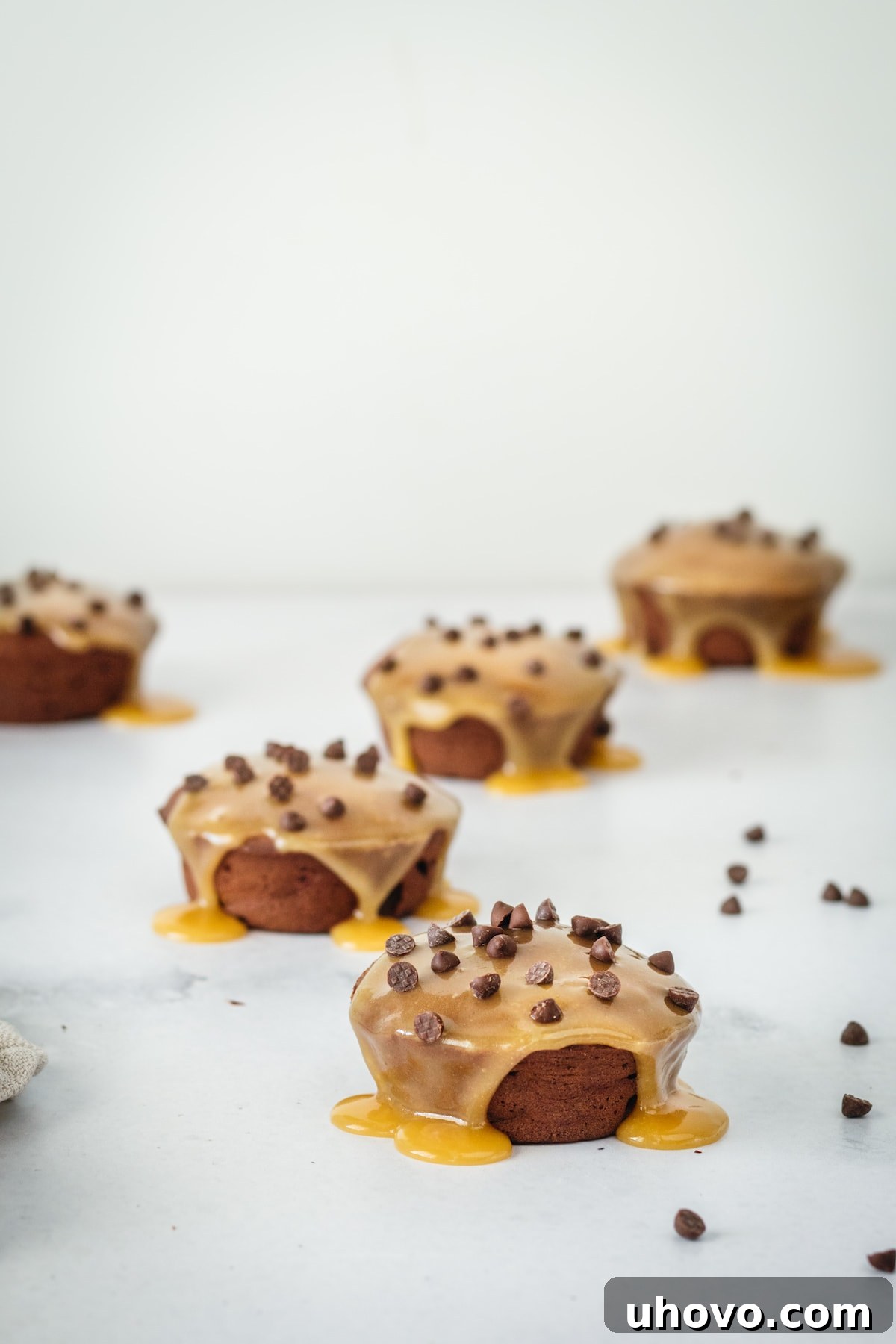 Mini chocolate cakes on marble baking slab after being drizzled with butterscotch and chocolate chip topping