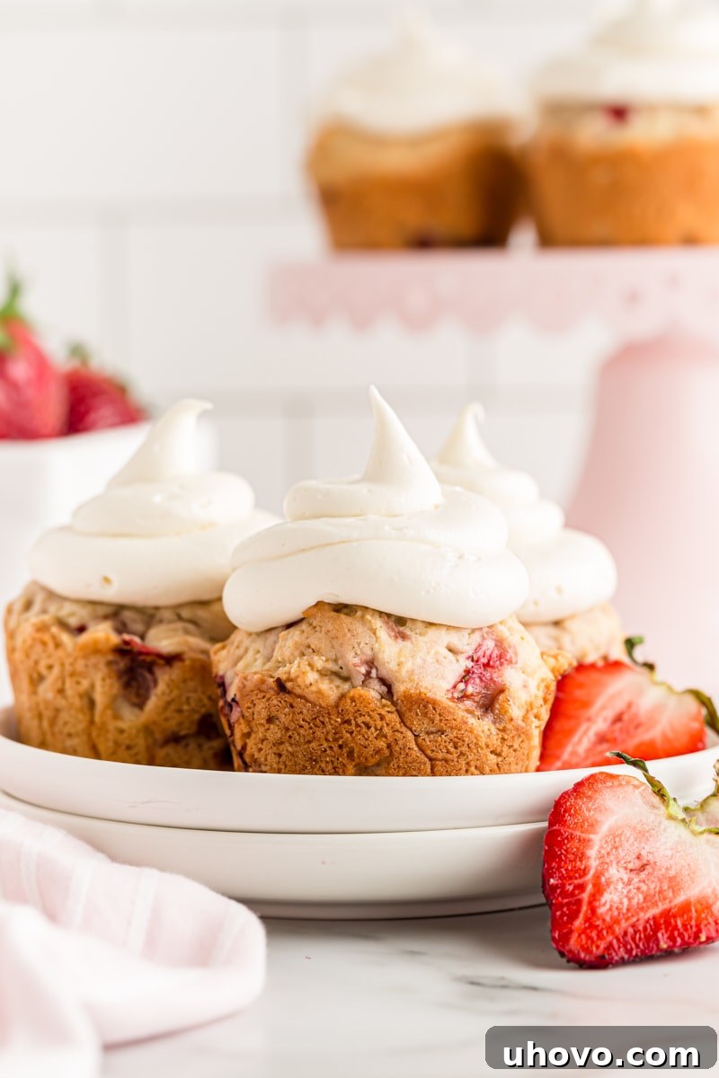 Three strawberry cupcakes on a plate with fresh strawberries, showcasing the moist cake and creamy white chocolate frosting