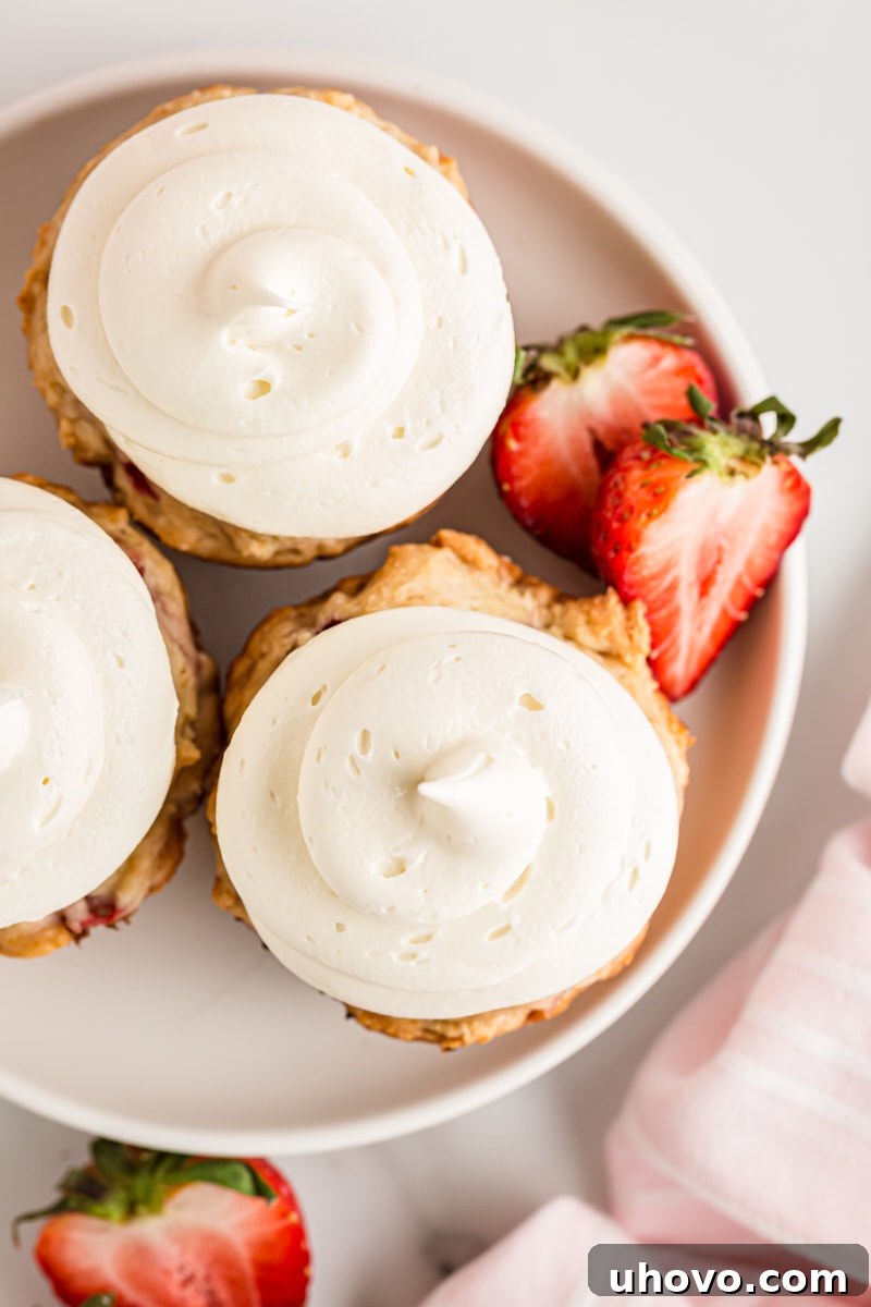 Overhead view of three perfectly frosted strawberry cupcakes arranged neatly on a pristine white plate