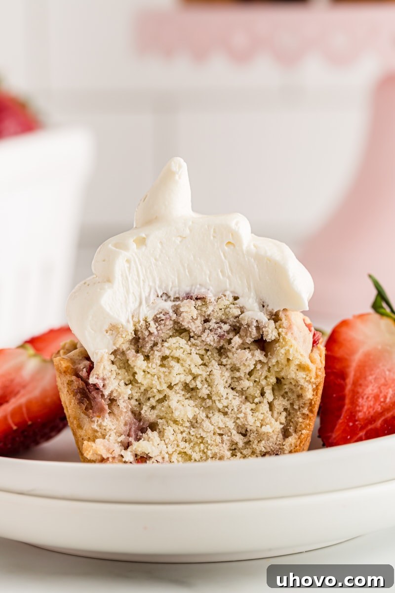 A halved strawberry cupcake on a plate, revealing the moist interior studded with strawberries and topped with white chocolate frosting
