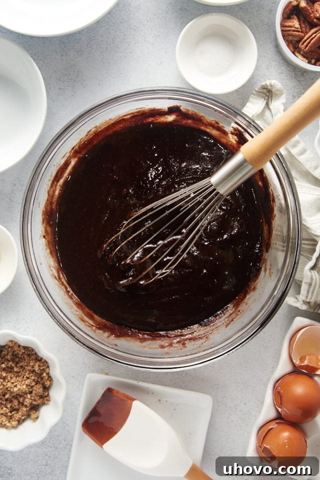 A close-up, overhead view of the brownie batter, partially mixed after eggs have been incorporated, showing a rich, dark consistency.