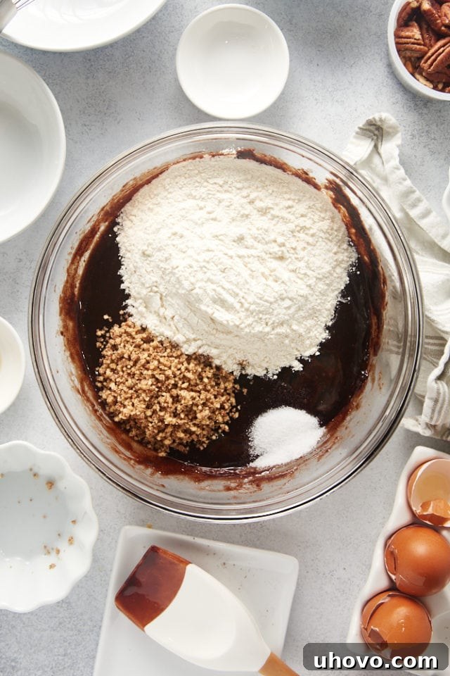 Overhead shot of flour, ground pecans, and salt just added to the brownie batter in a glass mixing bowl, before stirring.