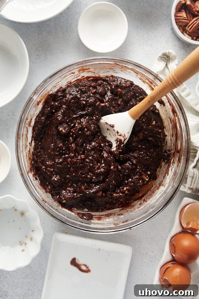 An overhead view of fully mixed brownie batter in a glass bowl, showcasing a thick, uniform consistency with visible pecan pieces and chocolate chips.