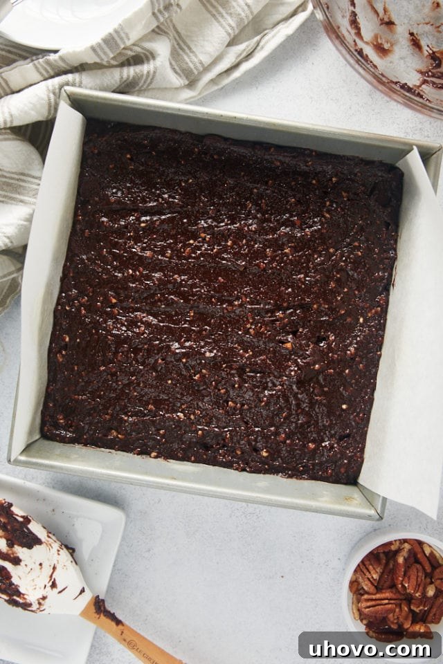 Overhead shot of rich brownie batter evenly spread in a parchment-lined square baking pan, ready for the next step.