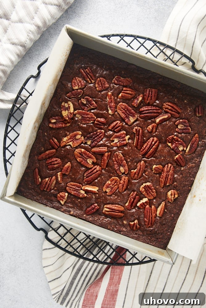An overhead view of a freshly baked batch of Pecan Lovers' Brownies still in the square baking pan, cooling on a wire rack, with their top crust and pecan topping clearly visible.
