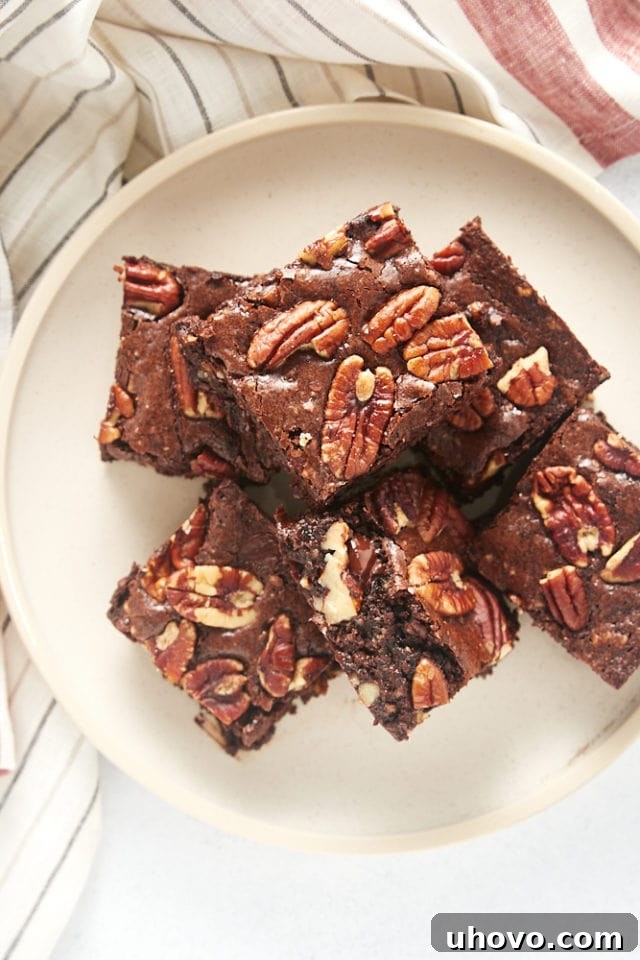 An inviting overhead view of a perfectly arranged pile of Pecan Lovers' Brownies on a beige plate, highlighting their rich texture and visible pecan toppings.