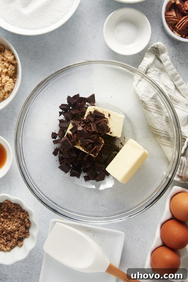 An overhead shot of solid chocolate chunks and cubes of butter in a clear glass mixing bowl, ready for melting.