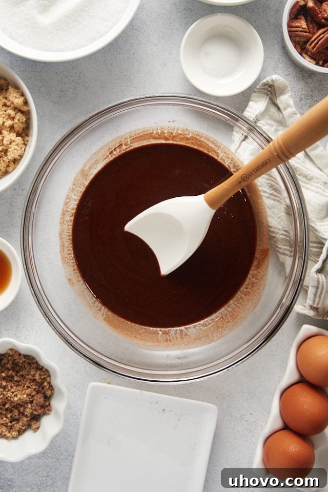 An overhead view of perfectly melted, glossy dark chocolate and butter swirled together in a clear glass mixing bowl, ready for the next steps.