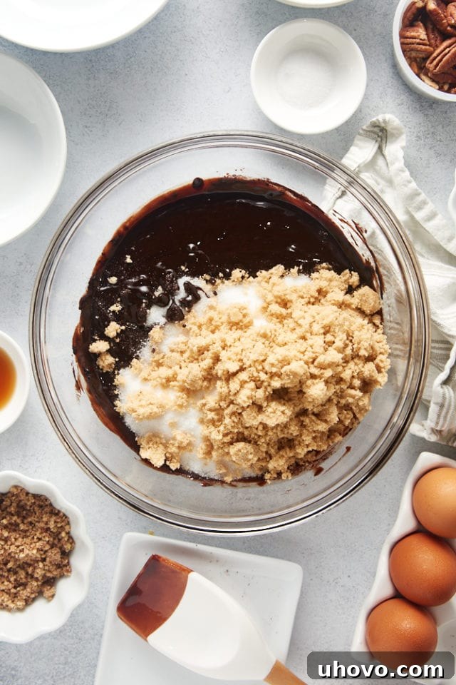 Granulated sugar and brown sugar freshly added to the brownie batter in a glass bowl, before being mixed in.