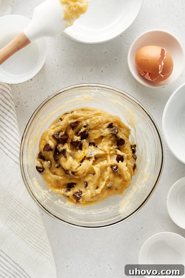 Overhead view of thoroughly mixed Deep Dish Chocolate Chip Cookie dough, rich with chocolate chips, in a glass mixing bowl, perfectly ready for portioning.